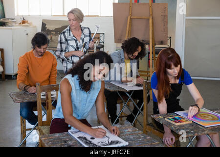 Female instructor examining students painting at table in art class Stock Photo