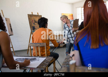 Female teacher examining students painting at table in art class Stock Photo