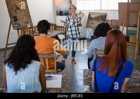 Teacher gesturing while explaining to students sitting at table in art class Stock Photo