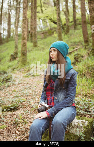 Thoughtful woman sitting on rock at forest Stock Photo