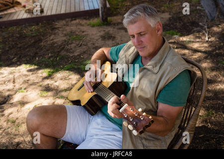 Mature man playing guitar while sitting on chair at campsite Stock Photo