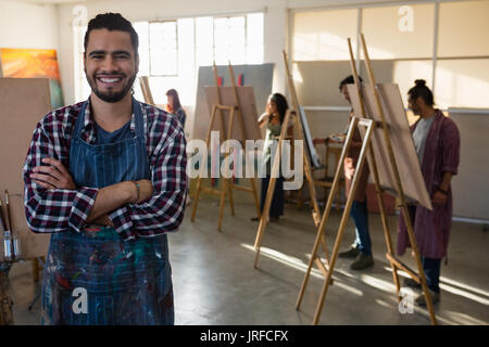 Portrait of smiling man with arms crossed standing against friends painting on easel Stock Photo