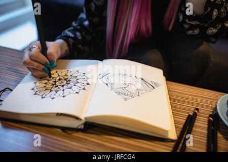Mid section of woman making design in book at cafe Stock Photo