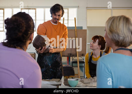 Male teaching holding sculpture while explaining students in art class Stock Photo