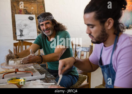 Portrait of teacher making clay pot on pottery wheel while sitting by student in art class Stock Photo