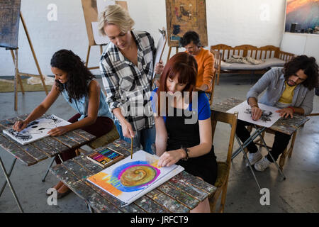 High angle view of instructor examining students painting at table in art class Stock Photo