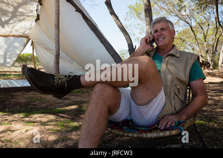 Mature man talking on phone while sitting on chair at campsite Stock Photo