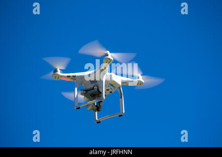 Drone or unmanned aerial vehicle in flight against blue sky Stock Photo