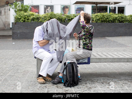 A couple shelter from a rain shower under their jackets at the Southbank, London, as the wet summer weather continues. Stock Photo