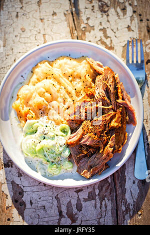 Pulled, seasoned pork, with mashed fried potatoes and cucumber and sour cream salad Stock Photo