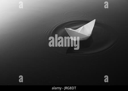 Paper boat floating on calm lake waters. Monochrome Stock Photo