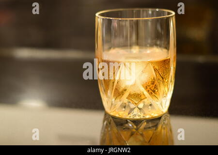 Gold and amber colored Whiskey on the rocks a in a crystal glass, with a giant melting cube of ice on a black granite bar. Stock Photo