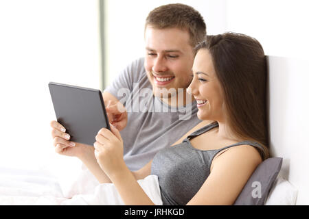 Couple watching media content together on line in a tablet on the bed of an apartment Stock Photo
