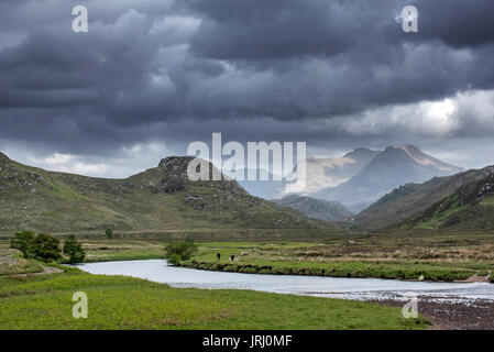 Two walkers walking on path along river and rain clouds forming in Wester Ross, Scottish Highlands, Scotland, UK Stock Photo