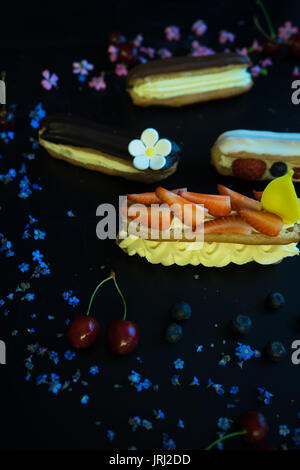 Different eclair dessert on dark wooden table decorated with strawberries and flowers Stock Photo
