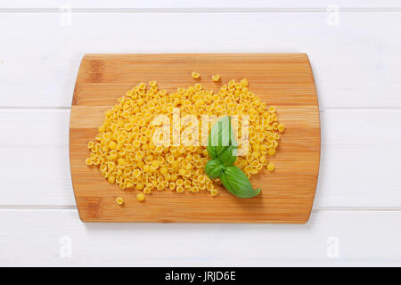pile of small pasta shells on wooden cutting board Stock Photo