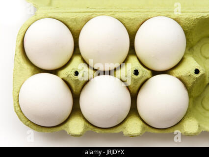 Six white eggs in a open green package, viewed from the top, against a white background closeup. Stock Photo