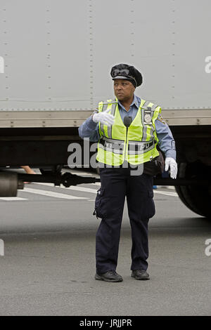 A policewoman in a safety vest and white gloves directing traffic on Canal Street in Chinatown, New York City. Stock Photo