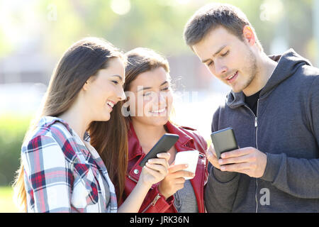 Three friends talking together and holding everyone their smart phones standing in the street Stock Photo