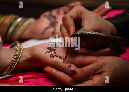 Detail of East Asian bride and mehndi artist's hands applying henna. Stock Photo