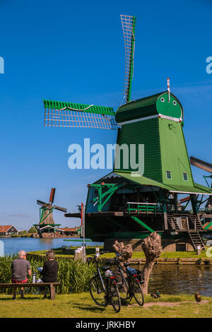 Rear view shot of senior couple sitting on a bench beside bicycles with windmills in the backgroud, Zaanse Schans, Netherlands, Europe Stock Photo