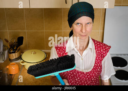 An angry and tired adult woman portrait, a housewife, a maid or maybe a witch, wearing a red apron and a green scarf on her head. She does not want to Stock Photo