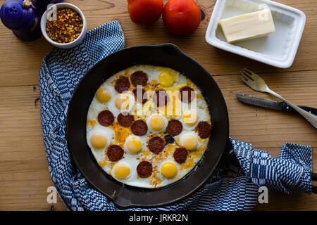 fried quail eggs with sausage in black pan Stock Photo