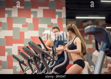 Side view portrait of sweaty fit woman exercising using elliptical machine during intense workout in modern gym Stock Photo