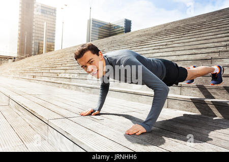Portrait of active young man doing push-up exercises outdoors on city stairs Stock Photo