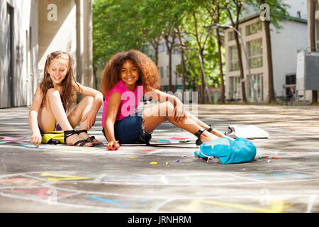 Two girls draw numbers for hopscotch game on the street Stock Photo