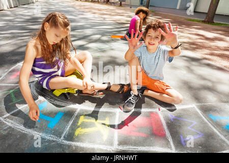 Kids draw with chalk on the road and happy handsome boy shows hands to the camera Stock Photo