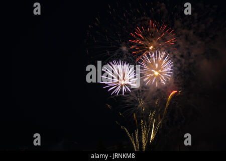 Brilliant fireworks display of red, yellow and white colors, set against a black sky during an evening of celebrating a national holiday. Stock Photo