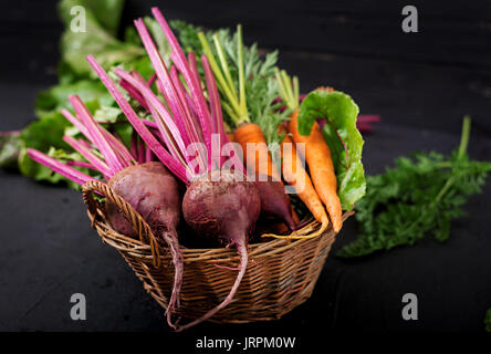 Young beetroot and carrots with a tops in a basket on a dark background. Stock Photo