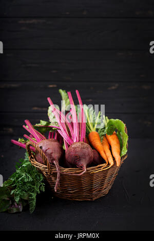 Young beetroot and carrots with a tops in a basket on a dark background. Stock Photo