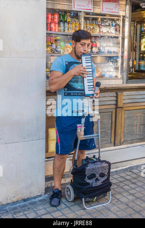 Street musician playing the pianica, also known as the melodica, blow-organ, key harmonica, or melodyhorn, on a sidewalk in Barcelona, Spain. Stock Photo