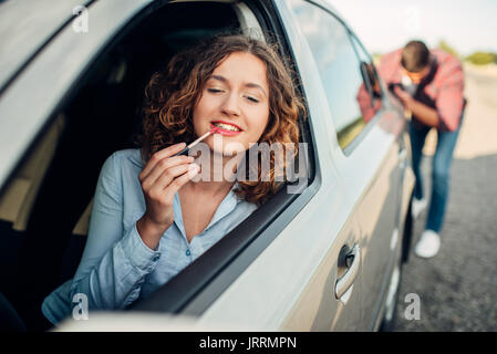 Man pushing a broken car down the road, woman driver. Vehicle with trouble Stock Photo