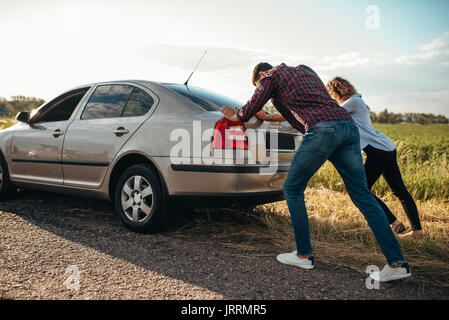 Man and woman pushing a broken car down the road, back view. Vehicle with trouble Stock Photo