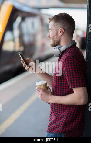 Man At Railway Station Using Mobile Phone On Platform Stock Photo