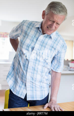 Mature Man Suffering From Backache Whilst Getting Out Of Chair At Home Stock Photo