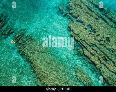 Aerial view of a canoe in the water floating on a transparent sea. Bathers at sea. Zambrone, Calabria, Italy. Diving relaxation and summer vacations. Stock Photo