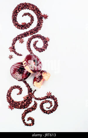 Coffee grains lying in the shape of a swirl with the cup, cinnamon, anise stars and donuts on a white background Stock Photo