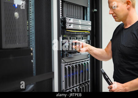 Confident mid adult male IT engineer installing hard drive in rack server at datacenter Stock Photo