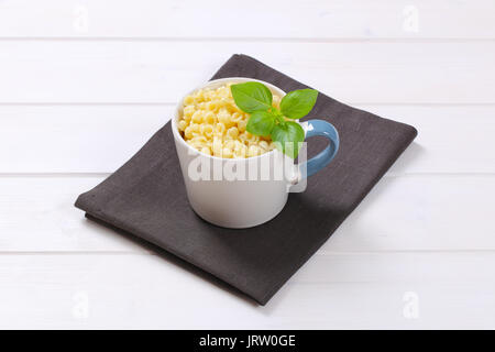 mug of small pasta shells on dark grey place mat Stock Photo