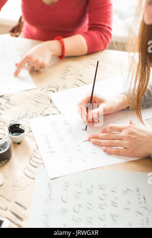 inspiration, patience, lettering concept. two women wearing grey and red sweatshirts creating various fonts with help of special equipment on the desk covered brown paper for sketching Stock Photo
