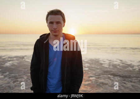 Young man in hoodie portrait on sea coast in sunset Stock Photo