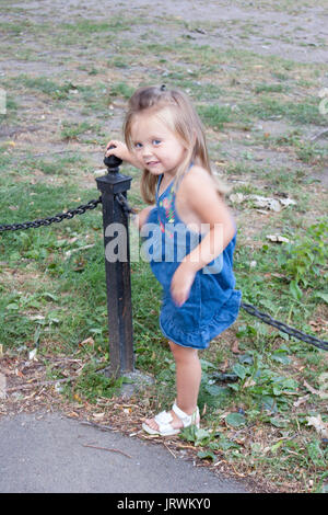 3-year old girl climbing over a fence in a park Stock Photo