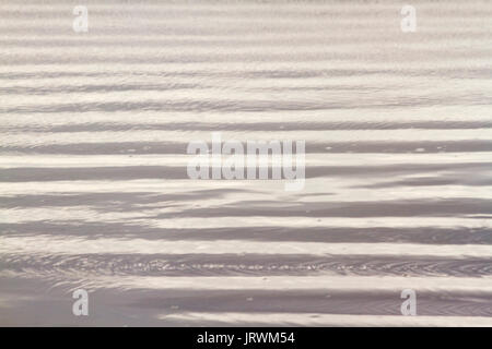 Close up photography of natural abstract patterns on the beach created by wet sand and small waves in the late afternoon sun Stock Photo