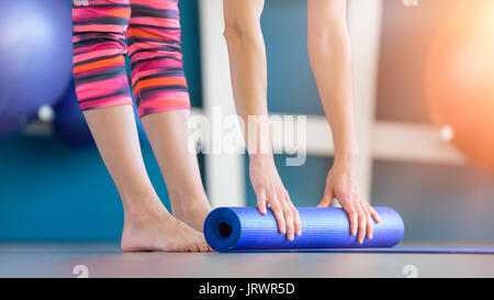Young woman folding blue yoga or fitness mat after working out. Healthy life, keeping fit concept. Stock Photo