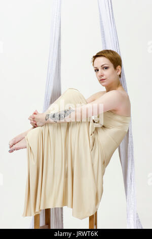 Authentic young woman dancing with aerial silks in dress on a chair Stock Photo