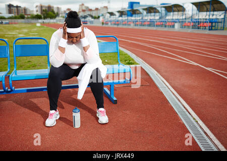 Chubby woman recovering after tough workout at track and field stadium Stock Photo